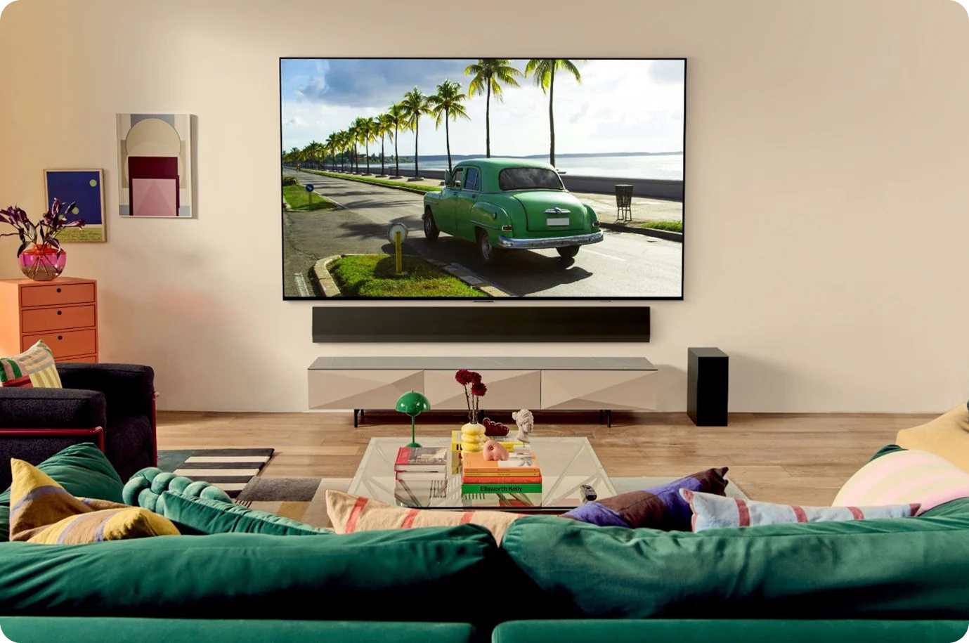Living room with a large TV displaying a green car on a beach, surrounded by furniture and decor.