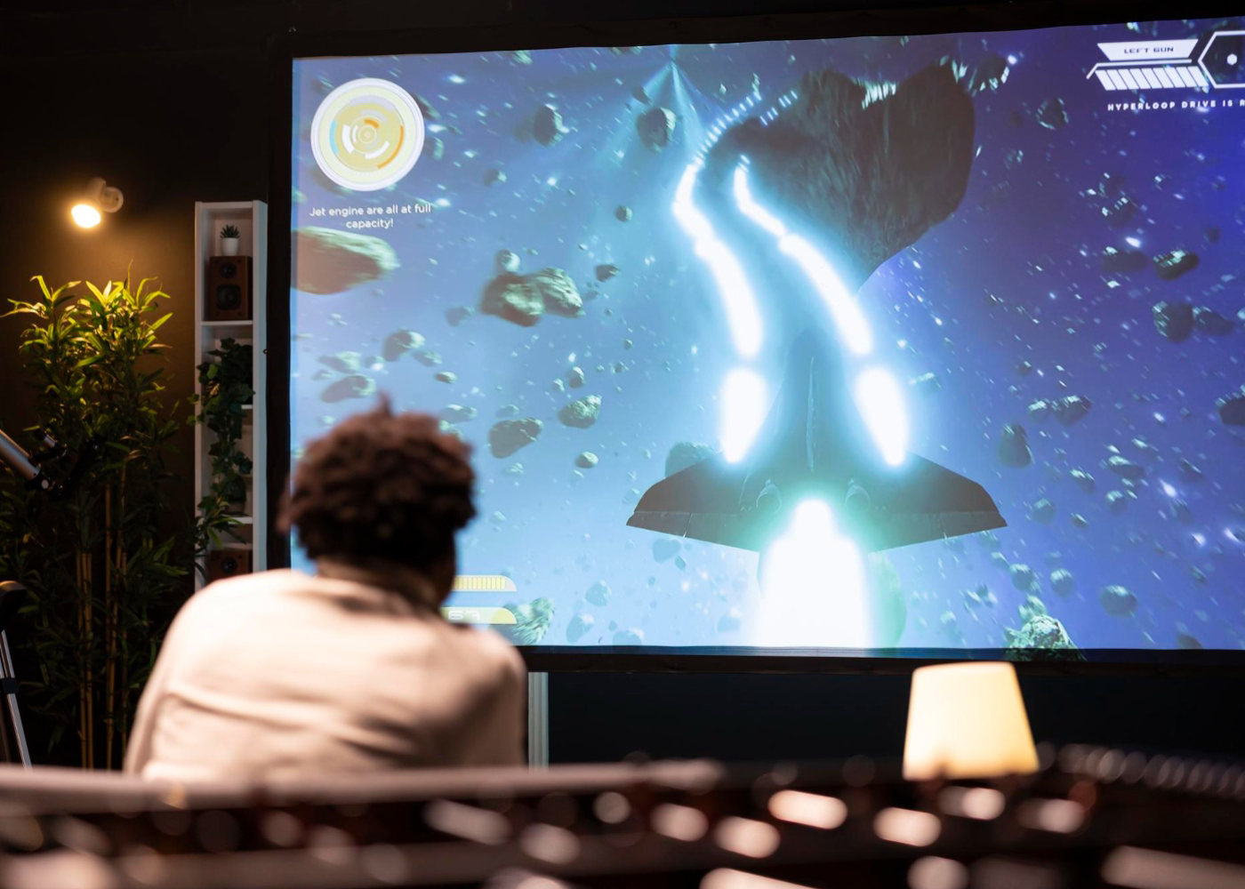 Person playing a space-themed video game on a large screen in a dimly lit room.