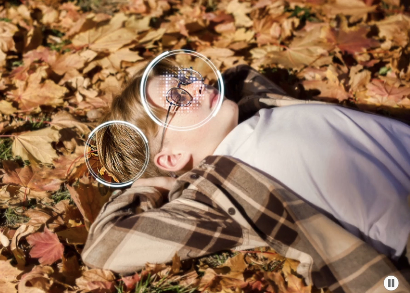 Person lying on autumn leaves wearing a plaid shirt and glasses.