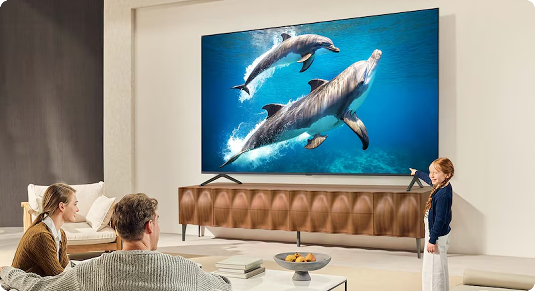 Family watching a large TV screen displaying dolphins in a living room.