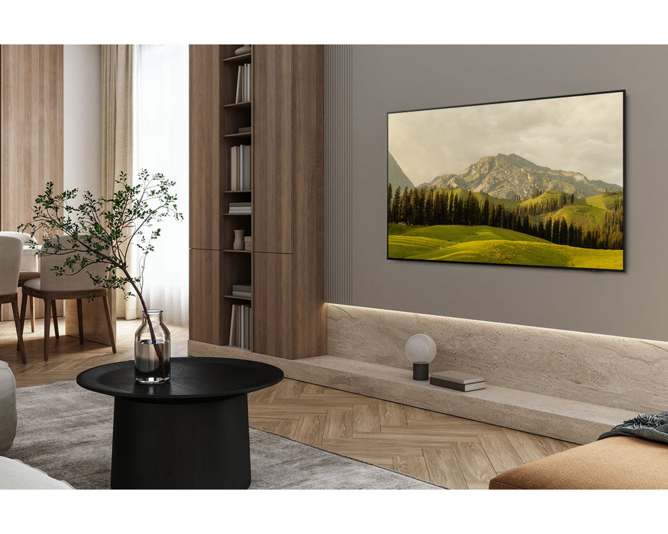 Modern living room with a large TV displaying a mountain landscape, a black round table, and a bookshelf.