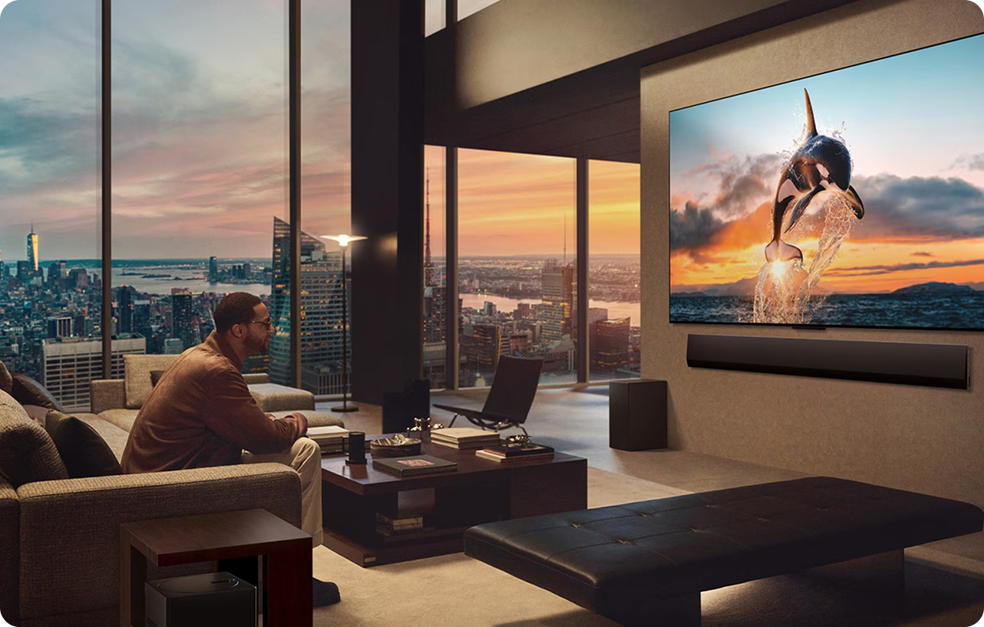 Man sitting in a modern living room with a large TV displaying a dolphin scene, overlooking a cityscape.